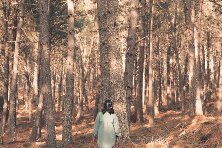 Young woman giving the back to the camera in the middle of a pine forest with copy space reflection...