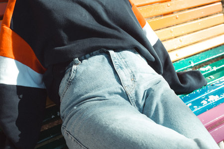 Close up of a woman wearing mom jeans over a rainbow lgbt bench at the park