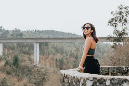 Young woman on sport clothes and sunglasses looking from a balcony with copy space during a sunny day, smiling to cameraの写真素材