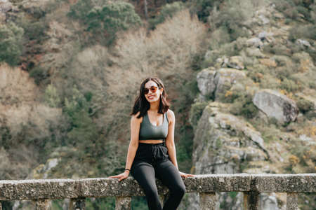 Young arab woman on sport clothes smiling using sunglasses while looking away from camera to a forest during an autumnal dayの写真素材