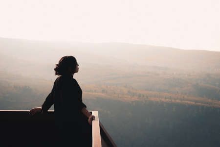 A young woman in front of massive mountains looking to the horizon during a sunny day wellness and liberty conceptの写真素材