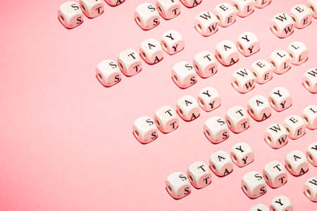 White dices over a pink pastel background with stay well message, repetitive pattern, minimalistic, wellness and life concepts with copy spaceの写真素材