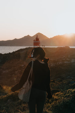 Woman in front of a red lighthouse during a colorful sunset using a mask, relax and confidence conceptsの写真素材