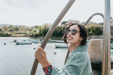 Young woman in a boat dock smiling during a sunny day while wearing sunglasses beach dayの写真素材