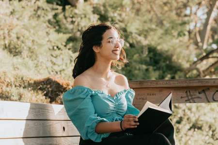 Young woman smiling to camera while reading at the beach during a super sunset while using a mask relax and inspirational concepts with copy space lifestyle colorfulの写真素材