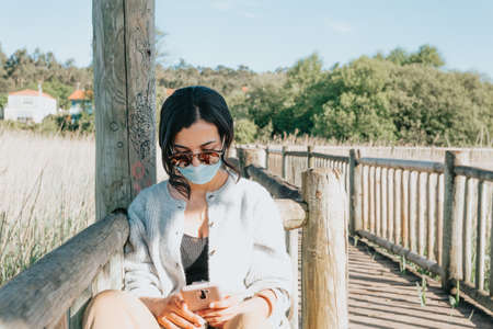 Young woman using sunglasses and a face mask while using a phone with copy spaceの写真素材
