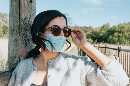 Woman using sunglasses and a face mask smiling to camera while in the country yard during a super sunny day with copy space and lifestyle shotの写真素材