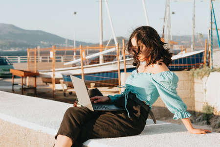 Young woman happy using his laptop on the docks during a super sunset during a super sunny day with copy space work outdoors conceptの写真素材