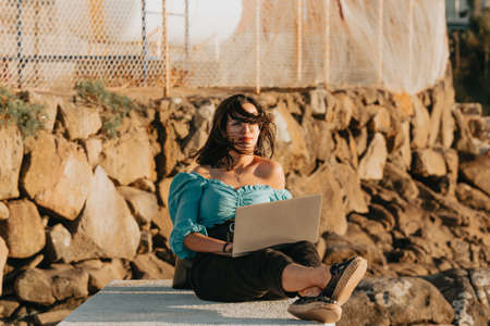 Young woman happy using his laptop on the docks during a super sunset during a super sunny day with copy space work outdoors conceptの写真素材