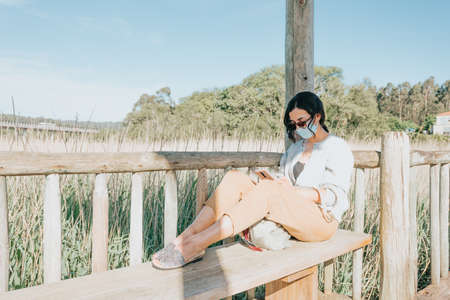 Young woman using sunglasses and a face mask while using a phone with copy spaceの写真素材