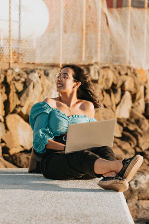 Young woman happy using his laptop on the docks during a super sunset during a super sunny day with copy space work outdoors conceptの写真素材