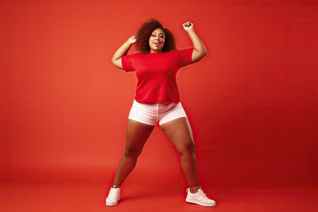 Plus size fit black african american woman enjoying a dance workout in a studio,color red backgroundの素材
