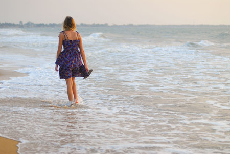 Beautiful young blond girl walking in the water on the beach