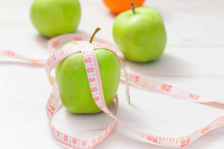Measuring tape wrapped around two green apple and orange isolated on white background, Concept of the goal to lose weight, the goal of dietの写真素材
