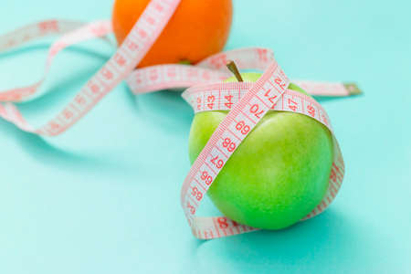 Measuring tape wrapped around two green apple and orange isolated on white background, Concept of the goal to lose weight, the goal of diet,の写真素材