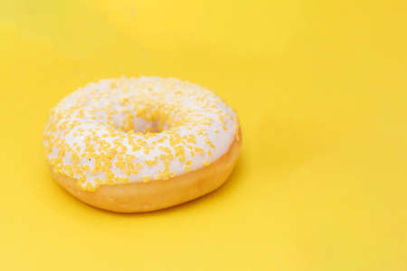 Donut with white sugar glazed and sprinkled with yellow pastry crumbs, on a yellow background with copy spaceの写真素材