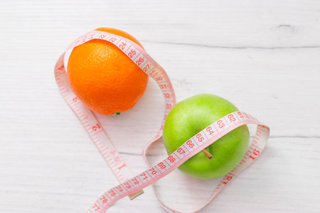 Measuring tape wrapped around two green apple and orange isolated on white background, Concept of the goal to lose weight, the goal of dietの写真素材