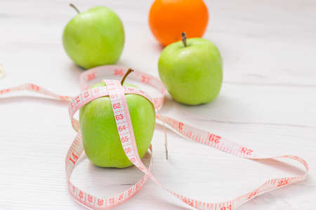Measuring tape wrapped around two green apple and orange isolated on white background, Concept of the goal to lose weight, the goal of dietの写真素材
