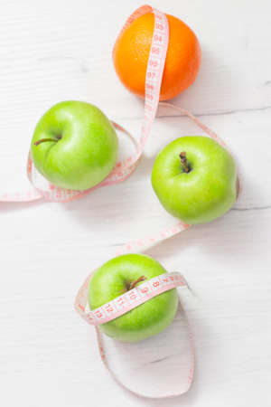 Measuring tape wrapped around two green apple and orange isolated on white background, Concept of the goal to lose weight, the goal of dietの写真素材