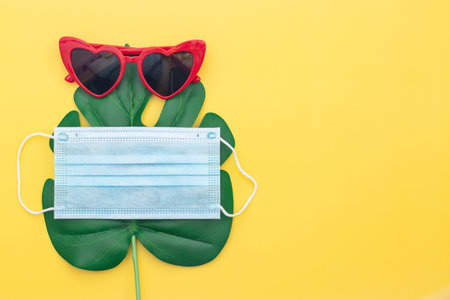 red sunglasses, green fern leaf and mask on table yellow