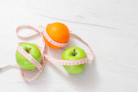 Measuring tape wrapped around two green apple and orange isolated on white background, Concept of the goal to lose weight, the goal of dietの写真素材