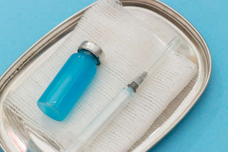 Concept of vaccination against coronavirus, medicine, injections, vaccination against covid-19. Bottle of vaccine on blue medical mask, syringe. Copy space. flat layの写真素材