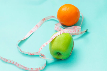 Measuring tape wrapped around two green apple and orange isolated on white background, Concept of...