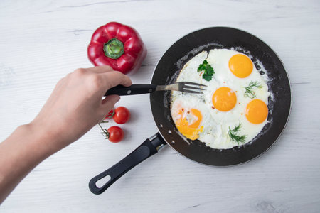 Scrambled eggs in frying pan bell pepper, cherry tomato on the background of a light wooden table. National Ukrainian or belorussian food. Breakfast, lunch. Top view, selective focus, rustic style.の写真素材