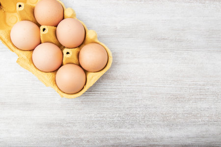 Large brown chicken eggs in yellowcarton packaging on wooden table. copy space