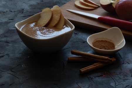 dessert of apple puree with grated cinnamon and cinnamon sticks accompanied by some red apples cut...