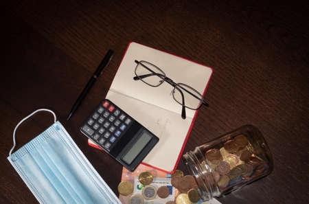 money from home savings in a glass jar and calculator and notebook after covid19 and mask confinementの写真素材