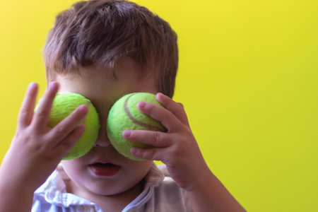 toddler playing places two tennis balls instead of eyes on a bright yellow and green pistachio backgroundの写真素材