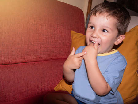 boy in blue pajamas playing on the red and yellow sofa at home without wanting to sleepの写真素材