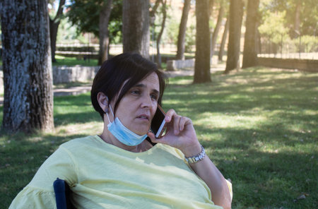 woman sitting in a camping chair in the countryside with her sanitary mask and worried calling the...
