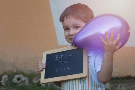 smiling toddler with a back-to-school letter board and playing with a purple balloon
