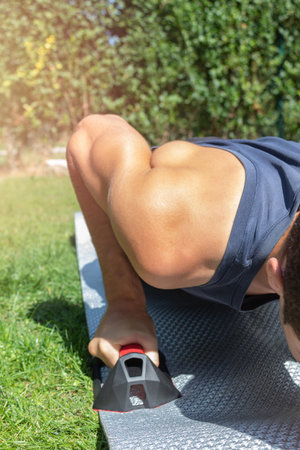 detail of the muscular arm of a boy with sports clothes doing crosstraining and push-ups with muscle...