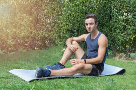 young fitness athlete sitting on the mat and resting having a small coffee and an energy bar to...