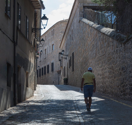 young man in shorts and sun hat climbing a hill in the streets of a Romanesque city on a sunny day