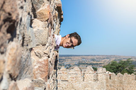 young boy sticking his head out of a part of the castle wall in a sunny landscapeの写真素材