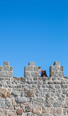 young man sitting and climbing the wall of a castle with copy space on a blue and sunny day