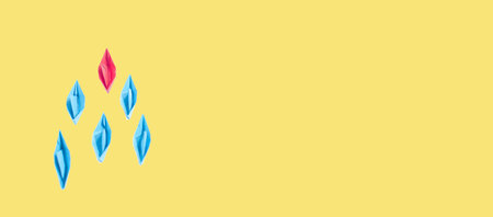 Leadership concept with pink paper boat leading among blue on yellow background.