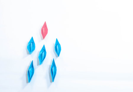 Leadership concept of a woman with pink paper boat leading among blues on white background.