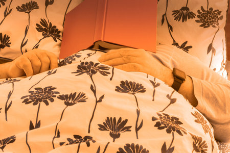 selective focus with a relaxed man with a book on his face lying on the bed at home tired and asleepの写真素材