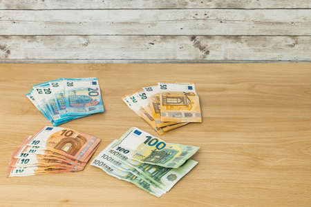 Several stacks of euro banknotes grouped by value of ten twenty fifty and one hundred on a wooden table finance and savings conceptの写真素材