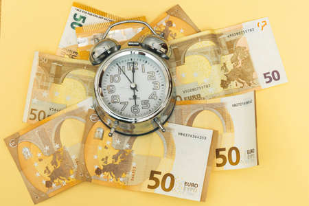 horizontal photo of a background of fifty euro banknotes and an analogical clock as time money work on yellow backgroundの写真素材