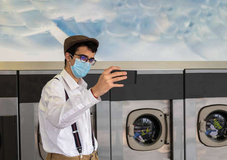 teenager taking a selfie with a cell phone while waiting for laundry to be cleaned in a heavy load washer.の写真素材