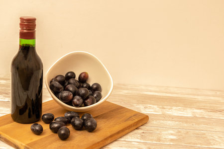 Selective focus of a bottle of red wine with red grapes in a bowl and on a wooden board from which...