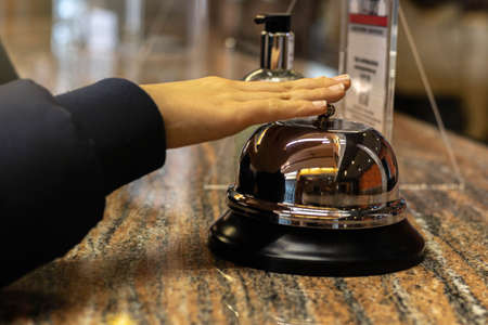 detail of a hand and a modern and luxurious hotel reception desk with silver-plated service bell for hotel checkout with selective focusの写真素材