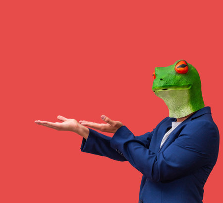 man with googly-eyed frog mask looking pointing and holding with both hands on red background with...