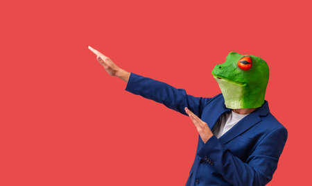 man with googly-eyed frog mask euphoric and celebrating with arms on red background with copy spaceの写真素材